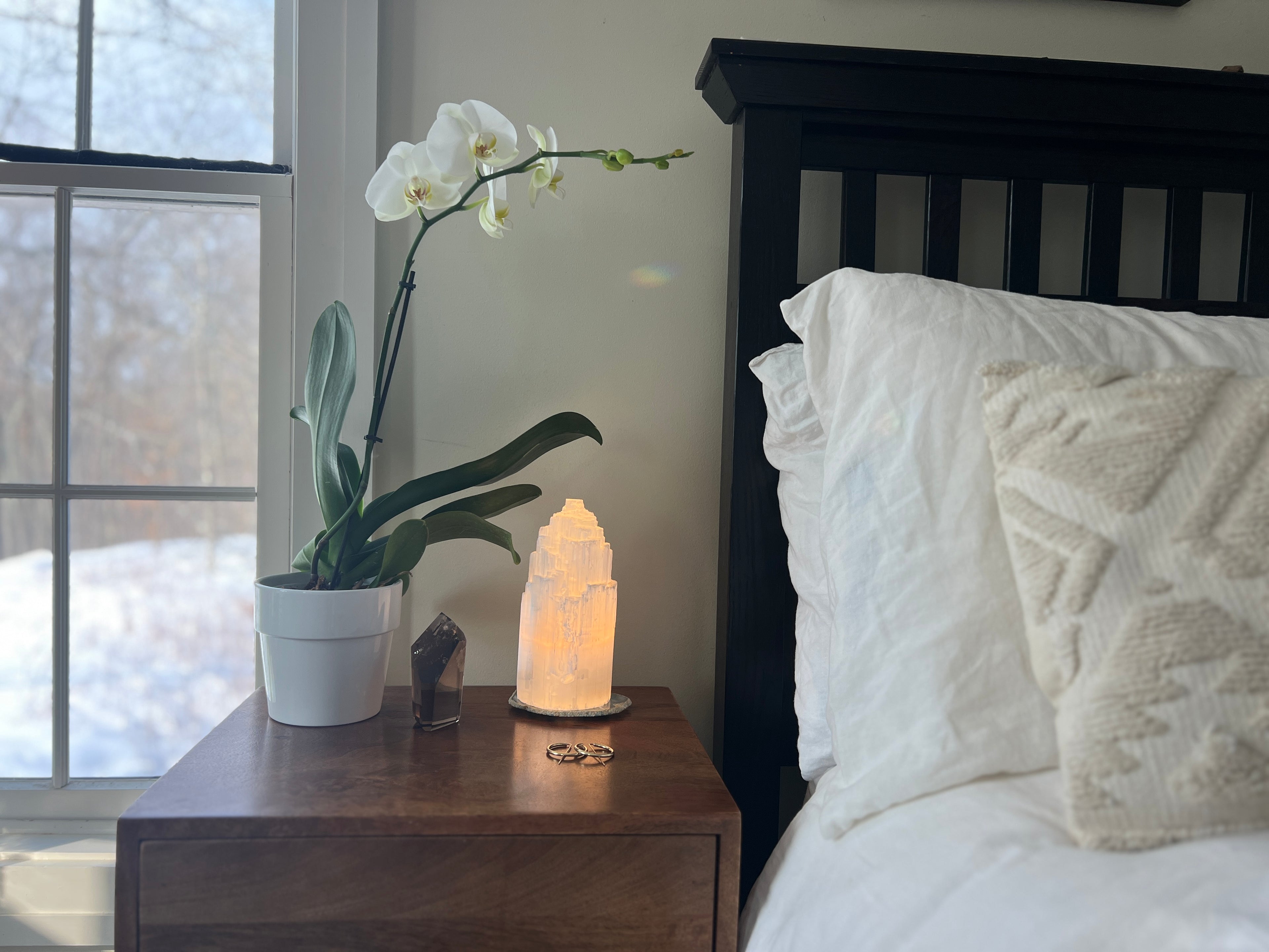 Bedroom white bedding with nightstand and an Orchid, Selenite Crystal Lamp, gold earrings